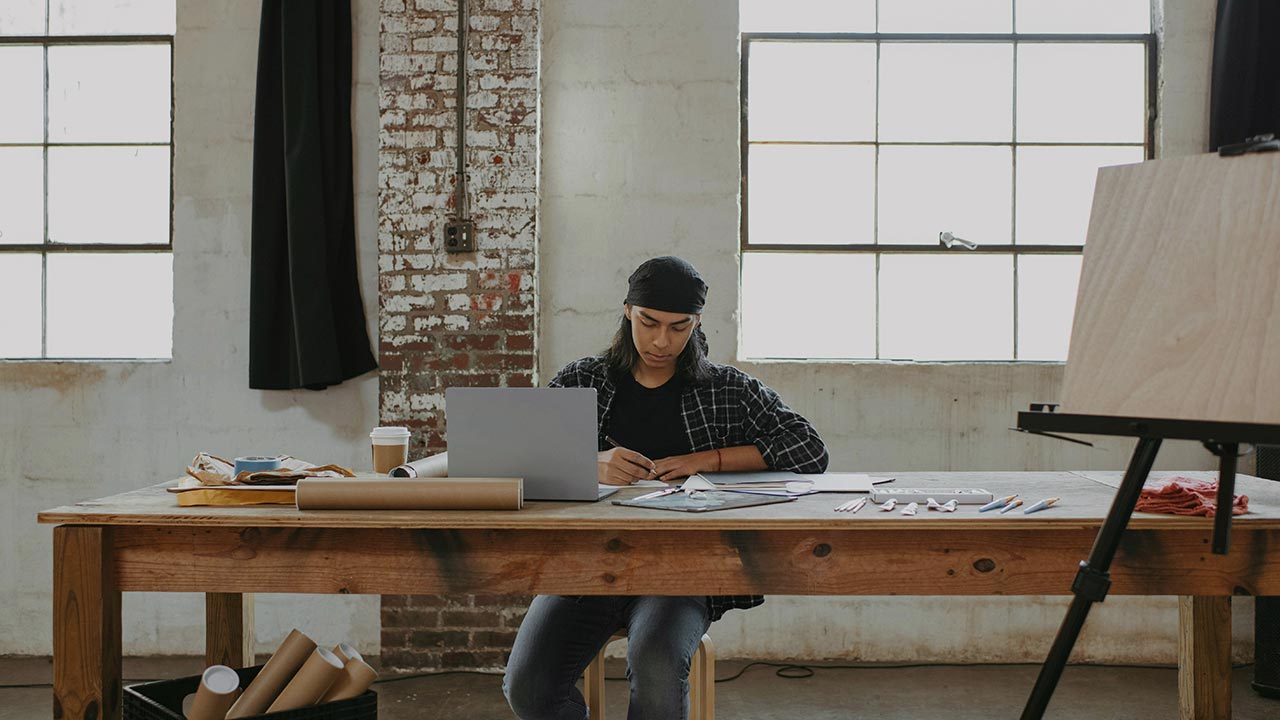 Mann sitzt auf einem Tisch mit Laptop und künstlerischem Werkzeug