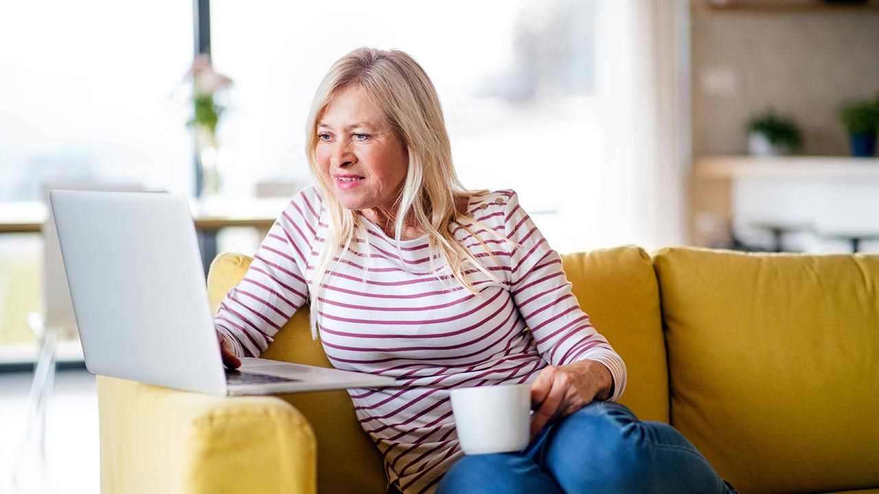 Ältere Frau sitzt mit Kaffeetasse vor Laptop