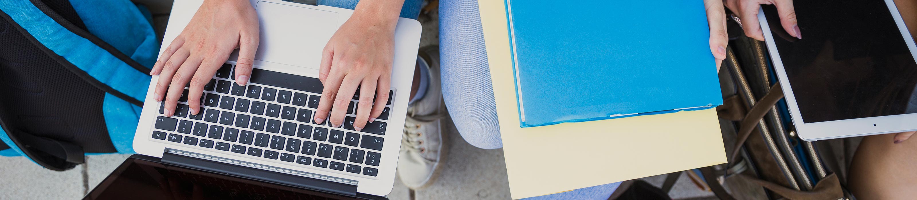 Hände auf einem Laptop und Bücher daneben