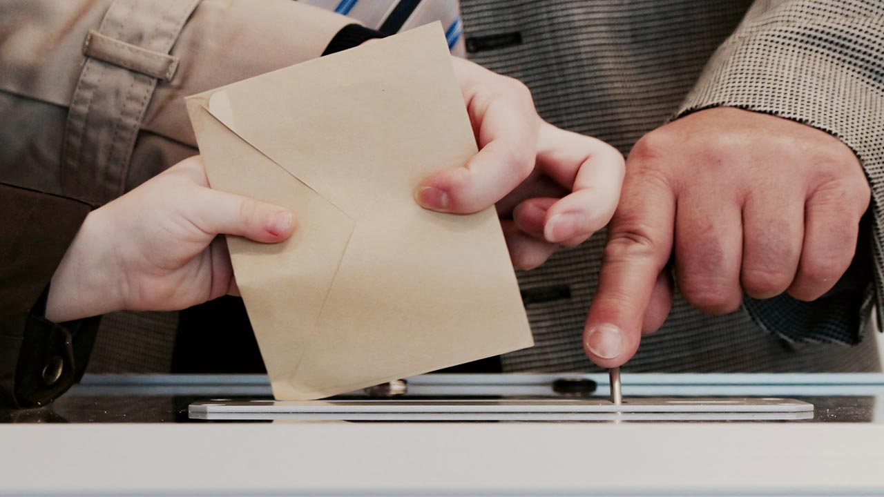 Drei Hände, die einen Stimmzettel in eine Box werfen